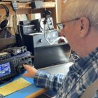 Phil Duggan sits at h is desk while operating ham radio controls.